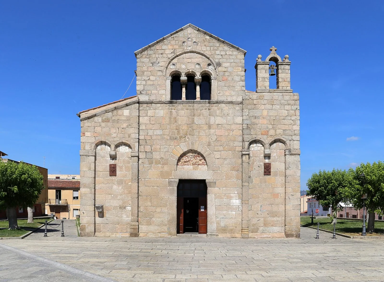 La facciata in granito della basilica romanica di San Simplicio a Olbia, con trifora e campaniletto a vela, sotto un cielo azzurro