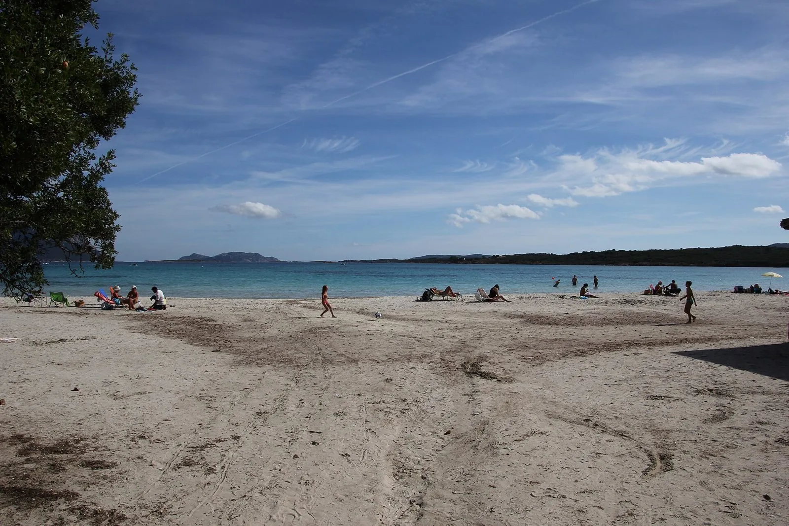 La spiaggia di Porto Istana con sabbia chiara, acqua turchese bassa e l'isola di Tavolara all'orizzonte, alcuni bagnanti in lontananza